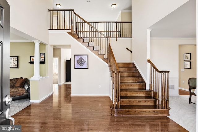 stairs with wood-type flooring, ornate columns, ornamental molding, and a towering ceiling