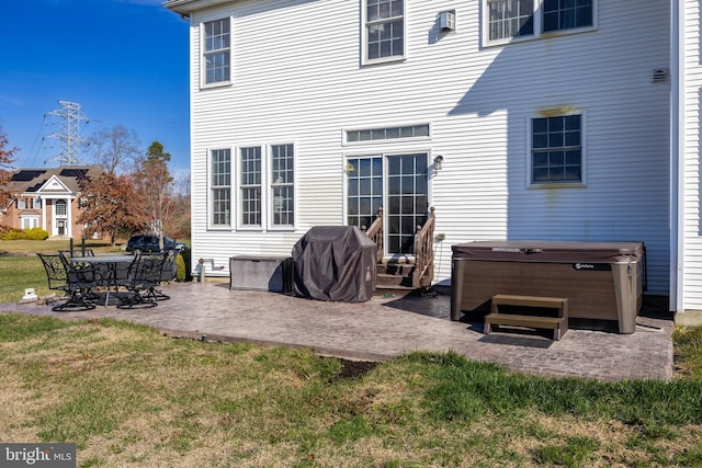 back of property with a yard, a hot tub, and a patio area