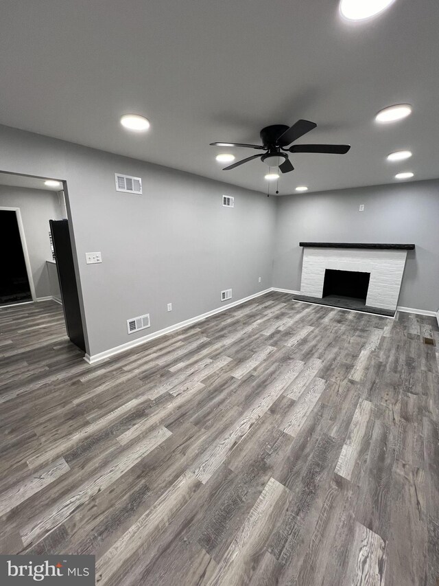 unfurnished living room with a brick fireplace, ceiling fan, and dark wood-type flooring