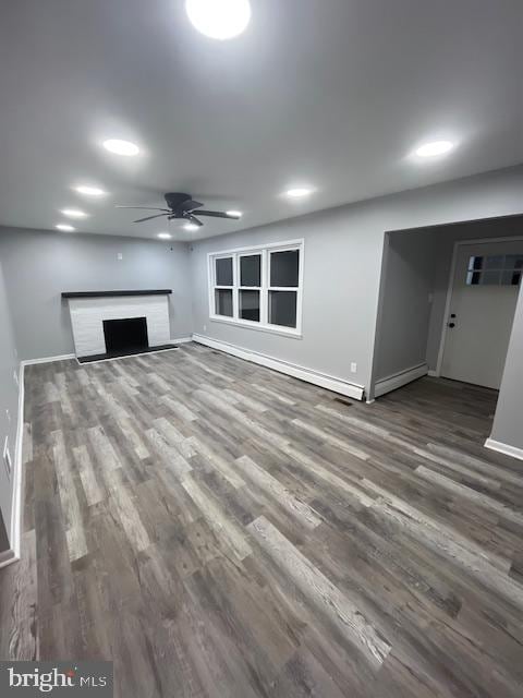 unfurnished living room with a baseboard radiator, hardwood / wood-style flooring, ceiling fan, and a brick fireplace