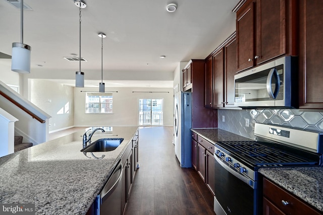 kitchen featuring light stone countertops, sink, hanging light fixtures, stainless steel appliances, and dark wood-type flooring