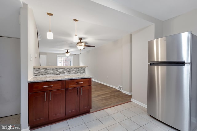 kitchen with light stone counters, stainless steel fridge, backsplash, light tile patterned floors, and ceiling fan