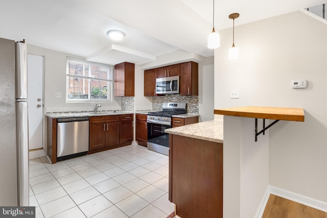 kitchen with kitchen peninsula, light stone counters, appliances with stainless steel finishes, tasteful backsplash, and pendant lighting