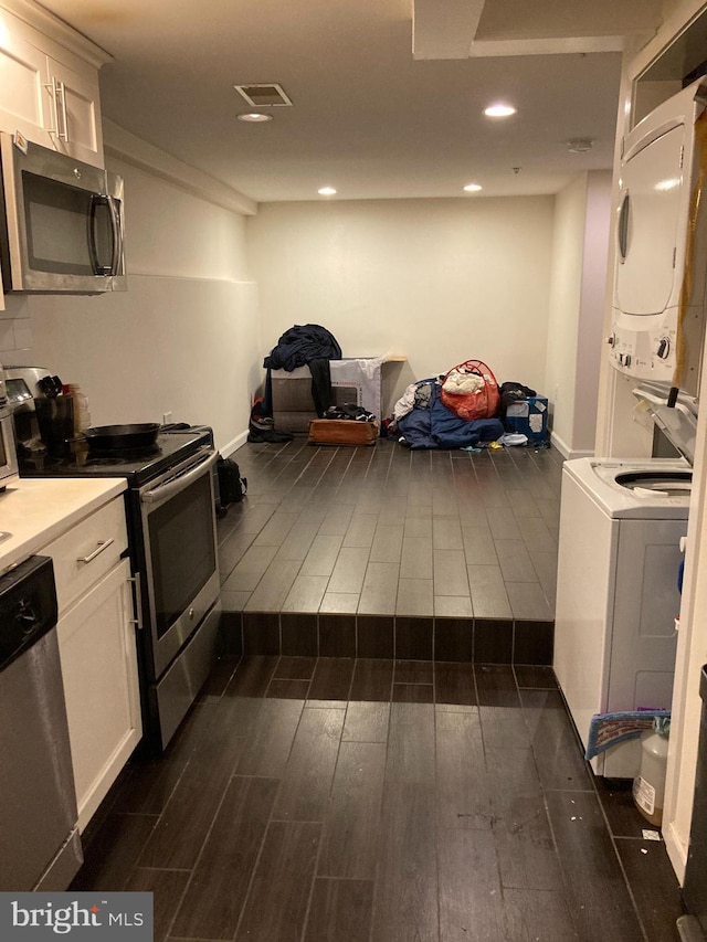 kitchen with dark wood-type flooring, stainless steel appliances, stacked washer and dryer, and white cabinets