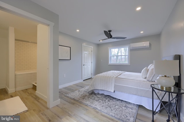 bedroom featuring ceiling fan, light wood-type flooring, a wall mounted AC, and ensuite bath