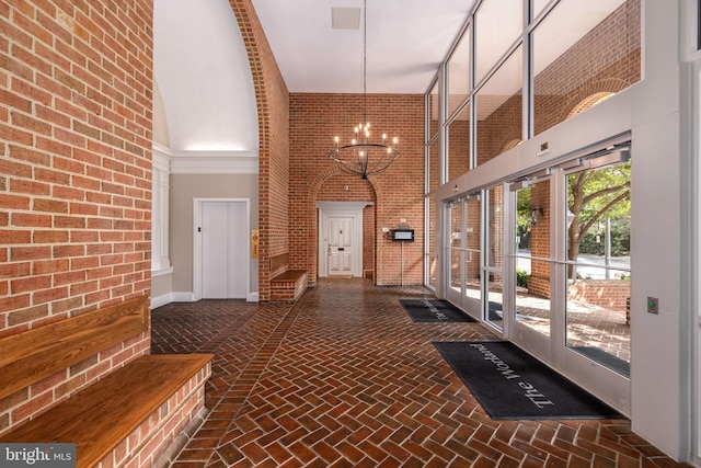 corridor featuring brick wall, a high ceiling, and a chandelier