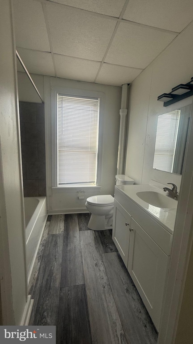 full bathroom with shower / washtub combination, hardwood / wood-style flooring, toilet, vanity, and a drop ceiling