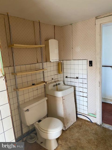 bathroom with toilet, tile walls, and sink