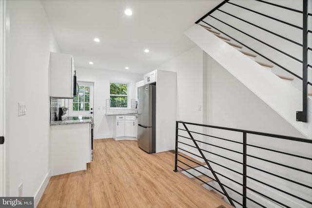 kitchen featuring appliances with stainless steel finishes, light stone countertops, white cabinetry, light hardwood / wood-style floors, and decorative backsplash