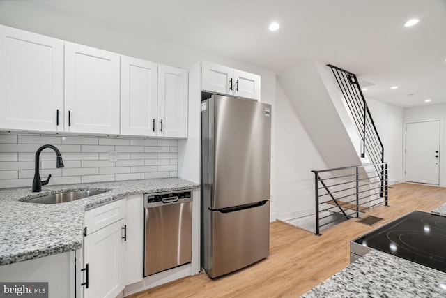 kitchen featuring light stone countertops, appliances with stainless steel finishes, sink, light hardwood / wood-style floors, and white cabinets