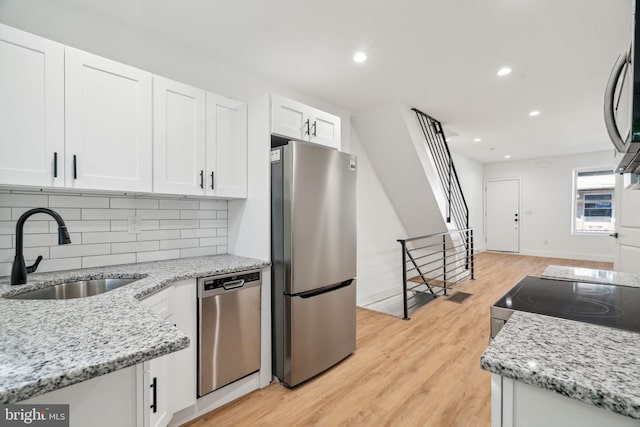 kitchen featuring decorative backsplash, white cabinets, light wood-type flooring, sink, and stainless steel appliances