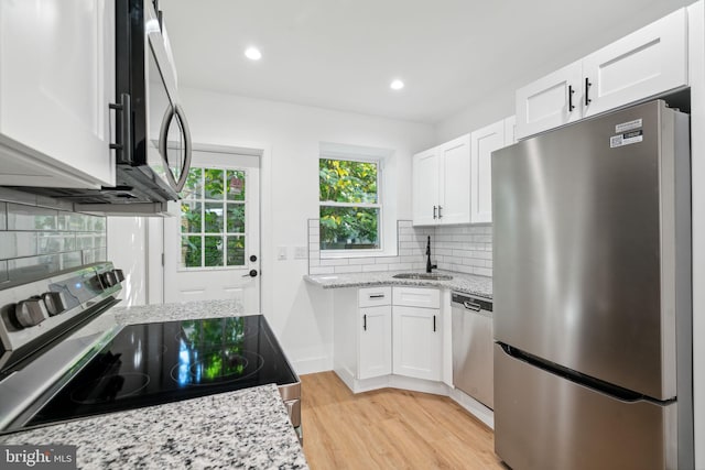 kitchen with sink, light wood-type flooring, backsplash, white cabinetry, and stainless steel appliances