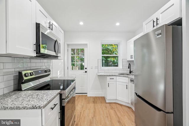 kitchen featuring light stone counters, appliances with stainless steel finishes, white cabinetry, light hardwood / wood-style flooring, and sink