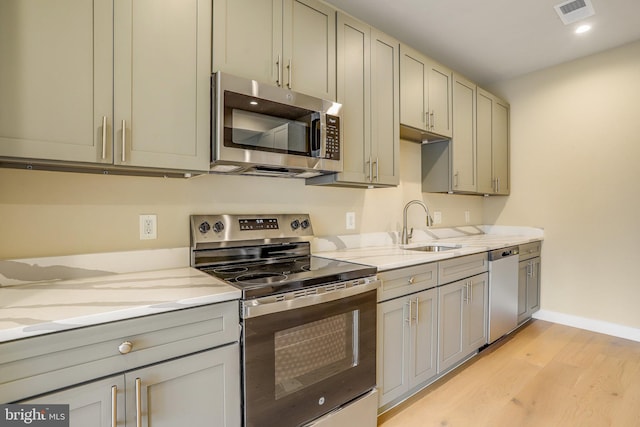 kitchen with light stone countertops, sink, light hardwood / wood-style floors, and appliances with stainless steel finishes