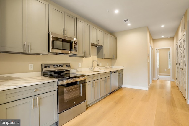 kitchen featuring gray cabinetry, sink, light stone counters, light hardwood / wood-style floors, and appliances with stainless steel finishes