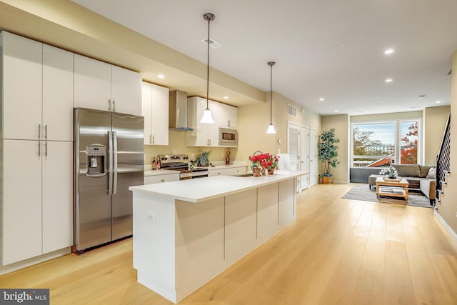 kitchen featuring appliances with stainless steel finishes, light hardwood / wood-style flooring, hanging light fixtures, and wall chimney exhaust hood