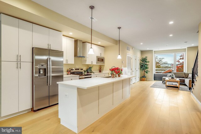 kitchen with light hardwood / wood-style flooring, decorative light fixtures, wall chimney range hood, and appliances with stainless steel finishes