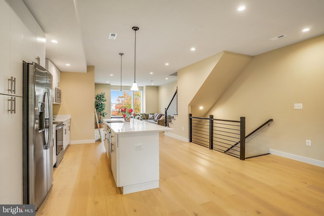 kitchen with white cabinets, hanging light fixtures, light hardwood / wood-style flooring, an island with sink, and appliances with stainless steel finishes