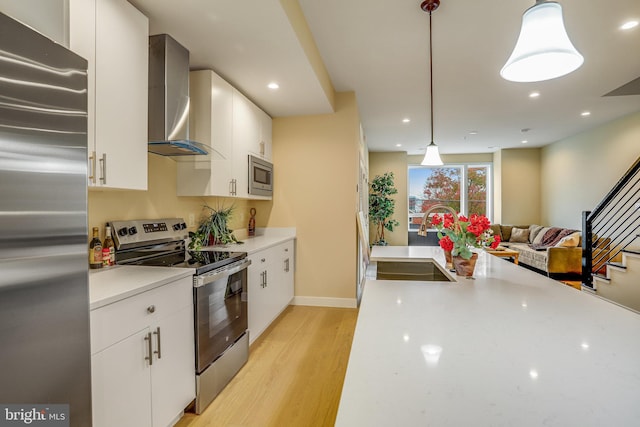 kitchen featuring pendant lighting, wall chimney exhaust hood, white cabinetry, and appliances with stainless steel finishes