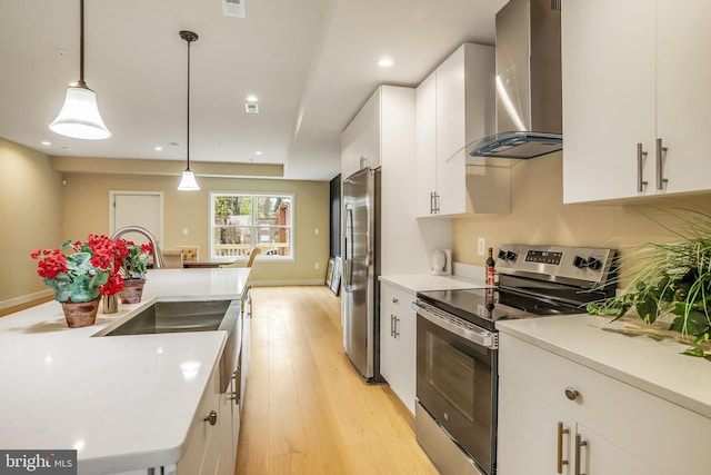 kitchen featuring pendant lighting, light hardwood / wood-style flooring, wall chimney exhaust hood, white cabinetry, and stainless steel appliances