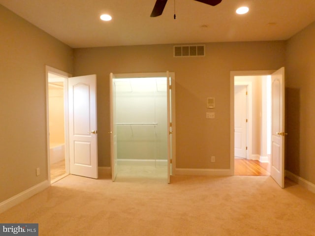 unfurnished bedroom with a walk in closet, light colored carpet, a closet, and ceiling fan