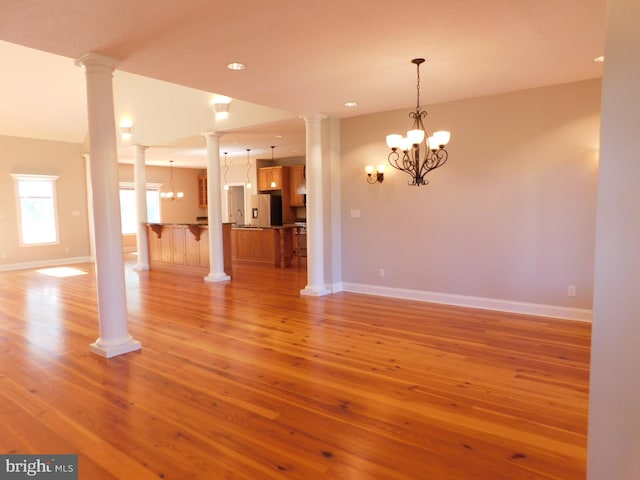 empty room with sink, a notable chandelier, hardwood / wood-style flooring, and ornate columns