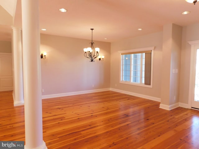 empty room featuring decorative columns, a notable chandelier, and wood-type flooring