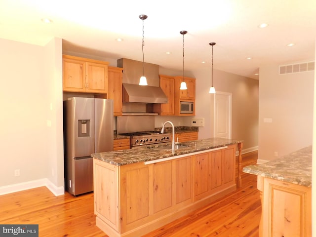 kitchen featuring appliances with stainless steel finishes, sink, hanging light fixtures, dark stone countertops, and light hardwood / wood-style flooring