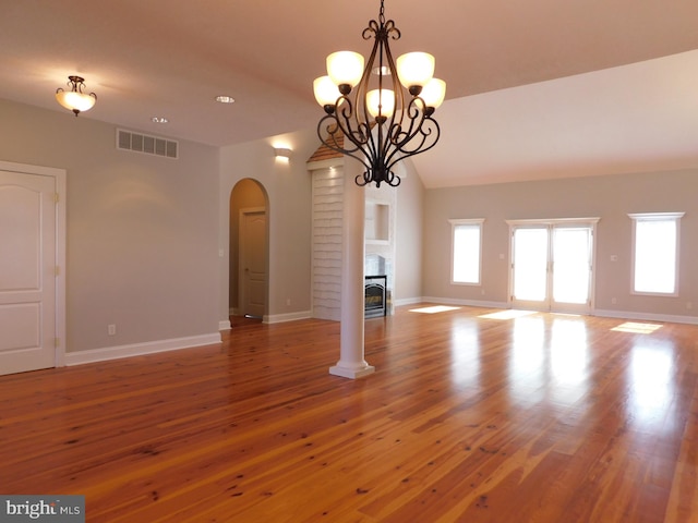 unfurnished living room featuring hardwood / wood-style flooring, lofted ceiling, a chandelier, and a fireplace