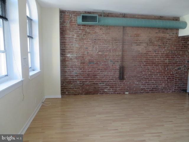 spare room with brick wall and light hardwood / wood-style floors