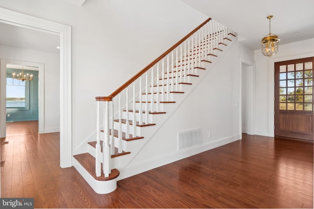 staircase with a notable chandelier, wood finished floors, visible vents, and baseboards