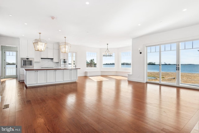 kitchen with a healthy amount of sunlight, an island with sink, decorative backsplash, wood finished floors, and white cabinetry