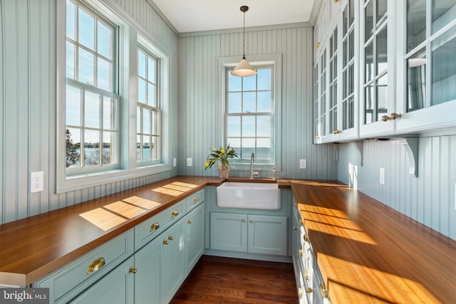 kitchen featuring blue cabinetry, dark wood-type flooring, butcher block countertops, pendant lighting, and a sink