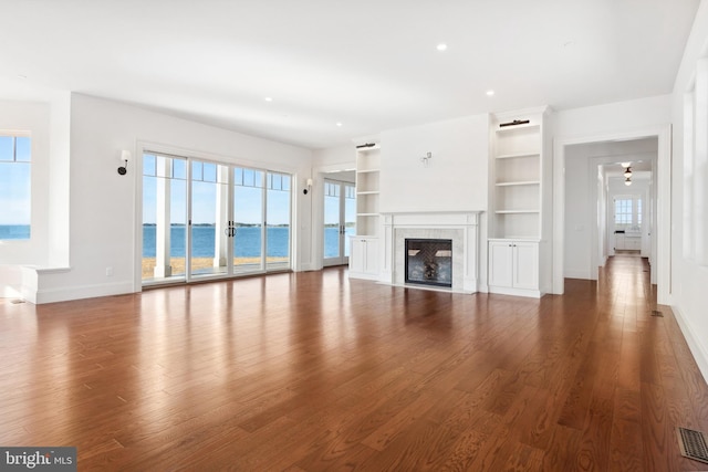 unfurnished living room with visible vents, a water view, wood finished floors, a high end fireplace, and baseboards