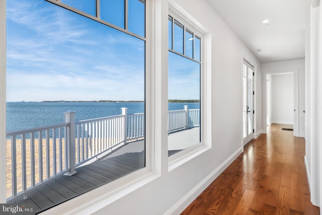 corridor with wood finished floors, a water view, and baseboards