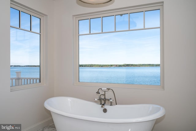 bathroom with a soaking tub, marble finish floor, baseboards, and a water view