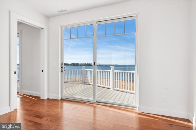 unfurnished room with wood finished floors, visible vents, a water view, and baseboards