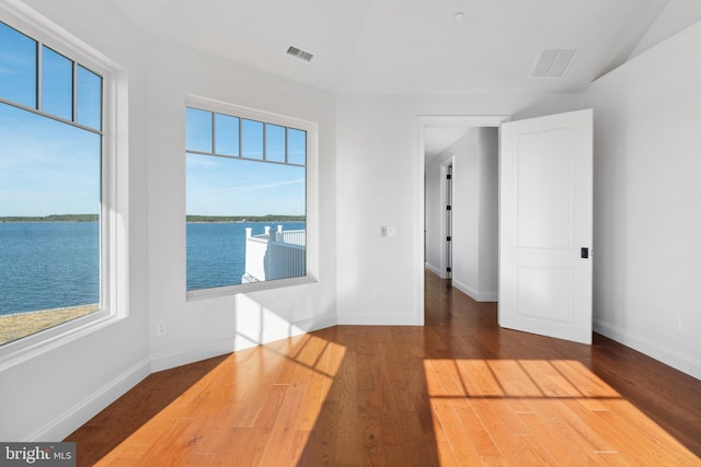 unfurnished room with visible vents, plenty of natural light, baseboards, and wood finished floors