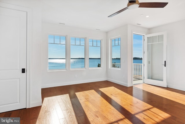 unfurnished room featuring visible vents, a water view, a ceiling fan, dark wood finished floors, and baseboards