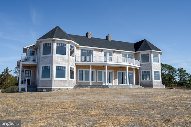 view of front facade with a shingled roof, a balcony, and a chimney