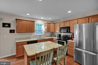 kitchen featuring sink, a center island, light hardwood / wood-style floors, a breakfast bar, and black appliances