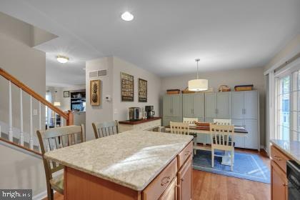 kitchen with dishwasher, a center island, light stone countertops, light wood-type flooring, and decorative light fixtures