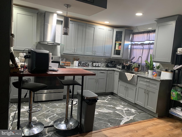 kitchen featuring light stone countertops, hardwood / wood-style flooring, gray cabinets, and wall chimney exhaust hood