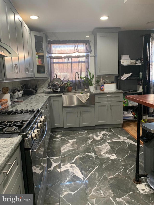 kitchen featuring light stone counters, gray cabinetry, wall chimney exhaust hood, gas stove, and sink