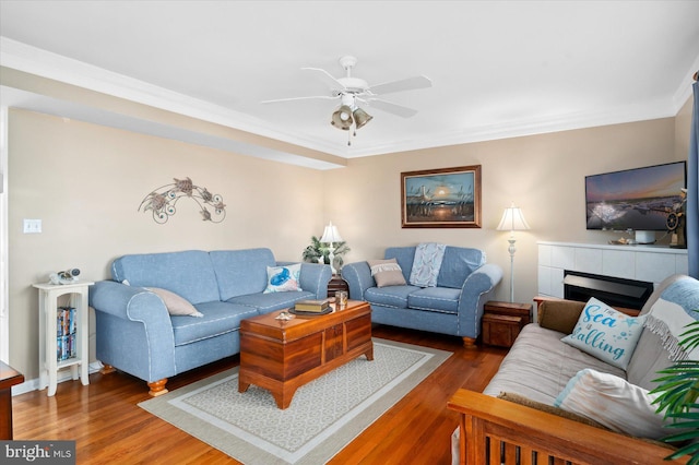 living room with ornamental molding, a tiled fireplace, dark hardwood / wood-style floors, and ceiling fan