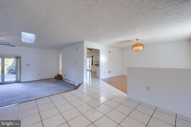 empty room with a skylight, a textured ceiling, baseboard heating, light tile patterned floors, and a chandelier