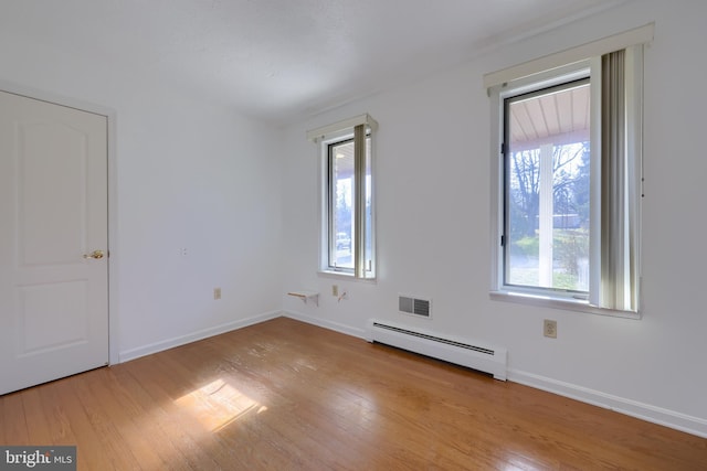 spare room featuring light wood finished floors, visible vents, baseboards, and a baseboard radiator