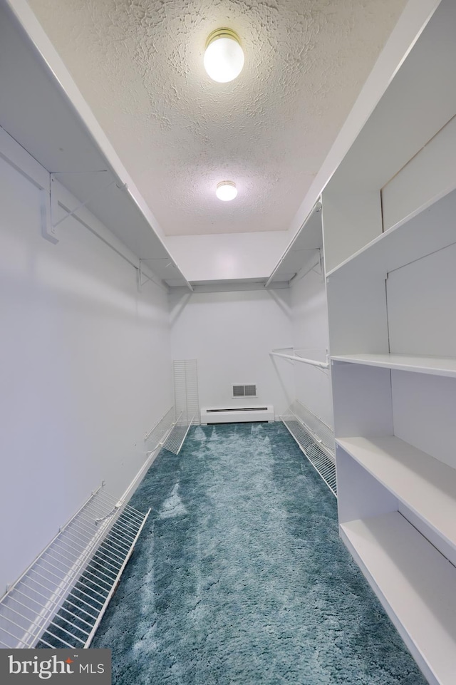 spacious closet featuring a baseboard radiator and dark colored carpet