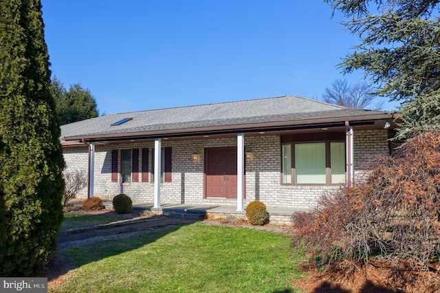 ranch-style home featuring a porch, a shingled roof, a front lawn, and brick siding