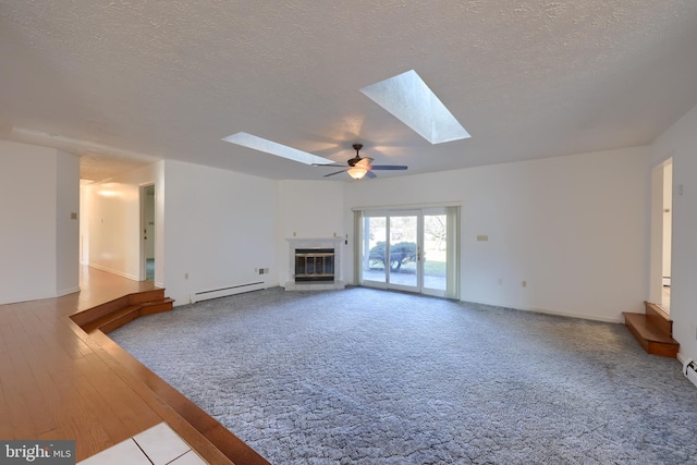 unfurnished living room with baseboard heating, wood-type flooring, ceiling fan, a textured ceiling, and a skylight